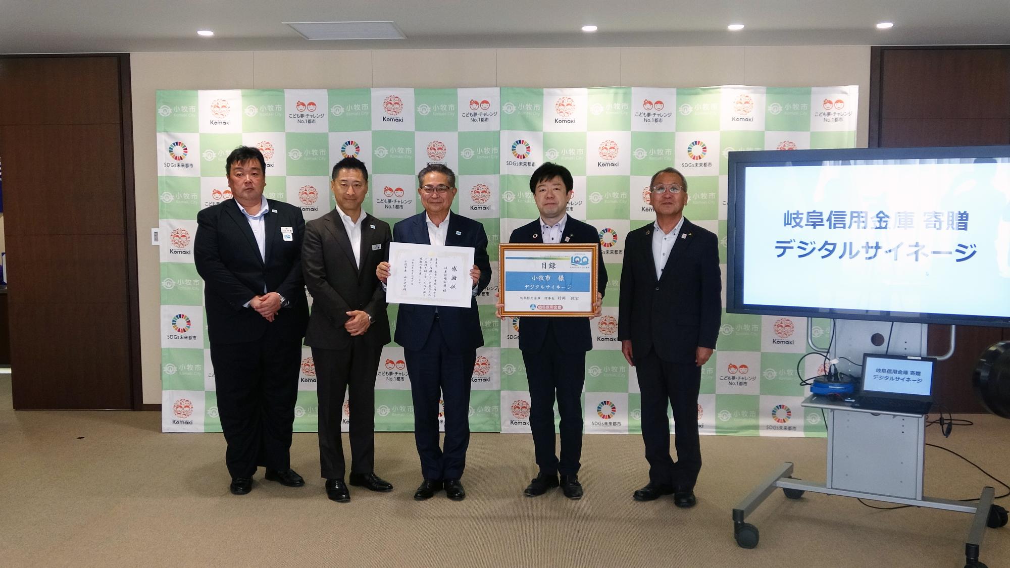 寄贈されたデジタルサイネージとともに写る岐阜信用金庫の皆さんと山下市長、中川教育長