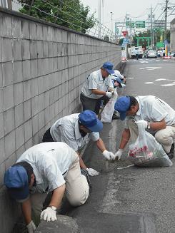 （写真）参加者男性達が、道路の溝のゴミを拾っている、三ツ星ベルトのクリーンアップ活動の様子