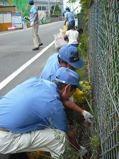 （写真）参加者男性達が道路脇の雑草やゴミを集める、三ツ星ベルトのクリーンアップ活動の様子