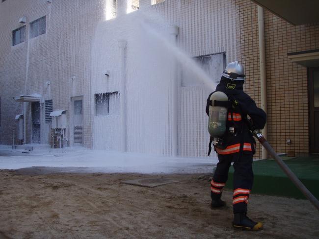 消防士が手に持ったホースで建物に向けて泡を放水している写真
