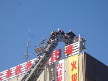 消防署の屋上へ伸びたはしごの先端にいる隊員の写真