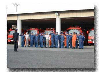 消防車の前で隊員達が代表者へ敬礼している写真