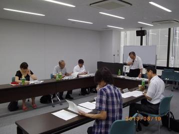 立ってマイクで話している委員長と資料を見ている委員の写真