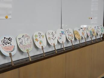 最終回に受講者が作った作品のうちわをホワイトボードに立てかけてある